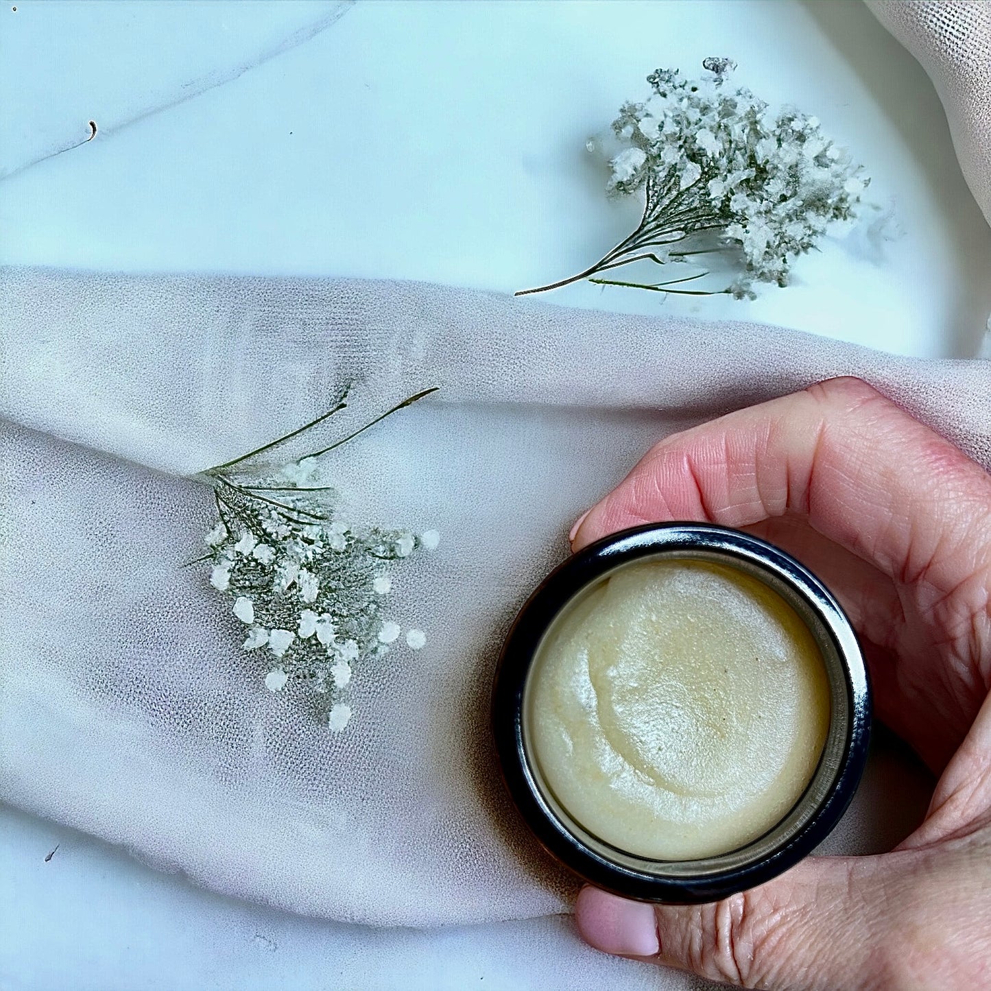 featuring a hand holding a glass jar of cleansing balm with the lid off made with oats and lavender and neroli essential oils made by buddha and bubbles botanicals