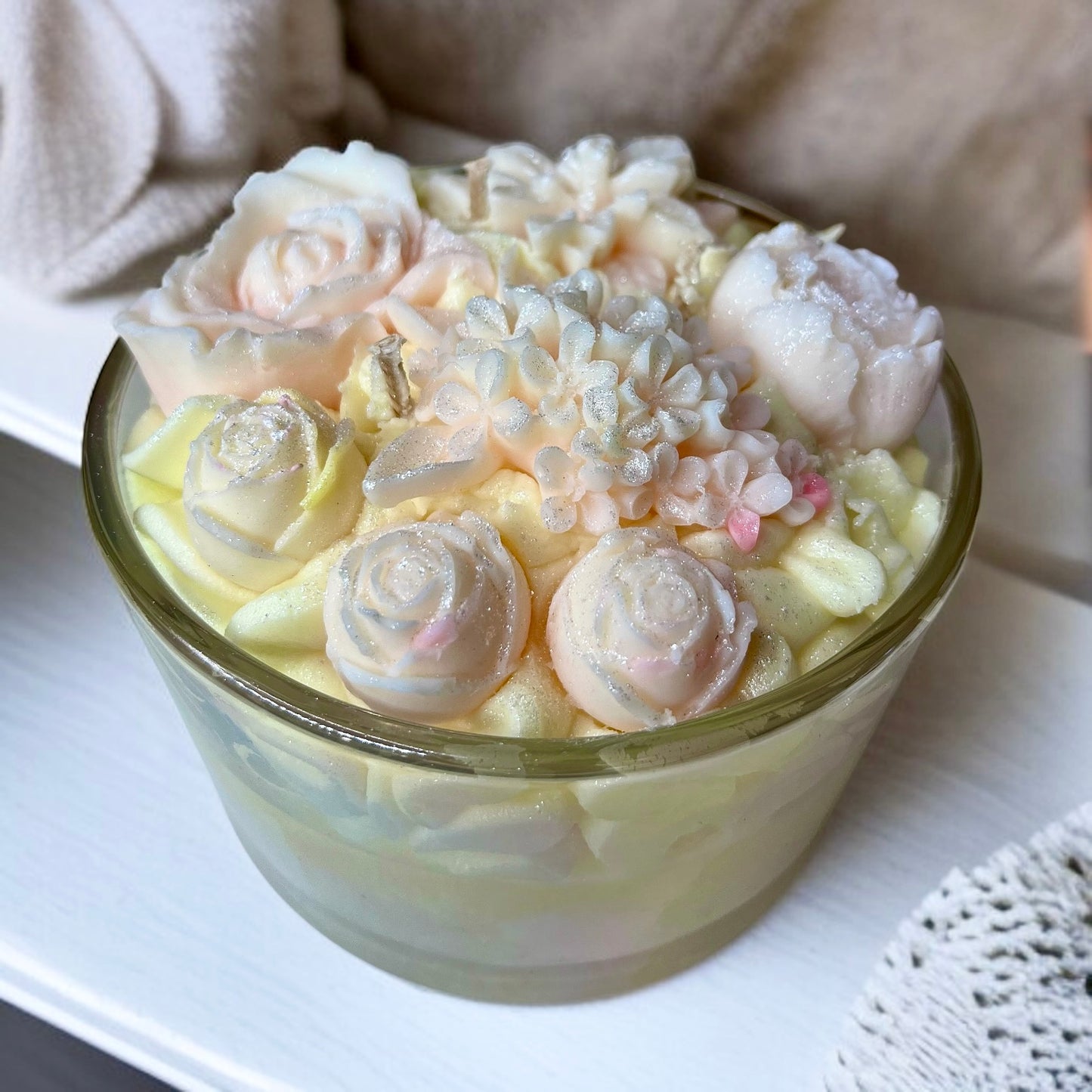 Decorative botanical candle with floral embed designs in a glass container on a white surface.
