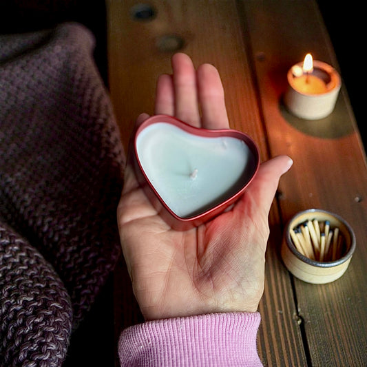 Heart-shaped candle held in a hand with a wooden surface and matches in the background