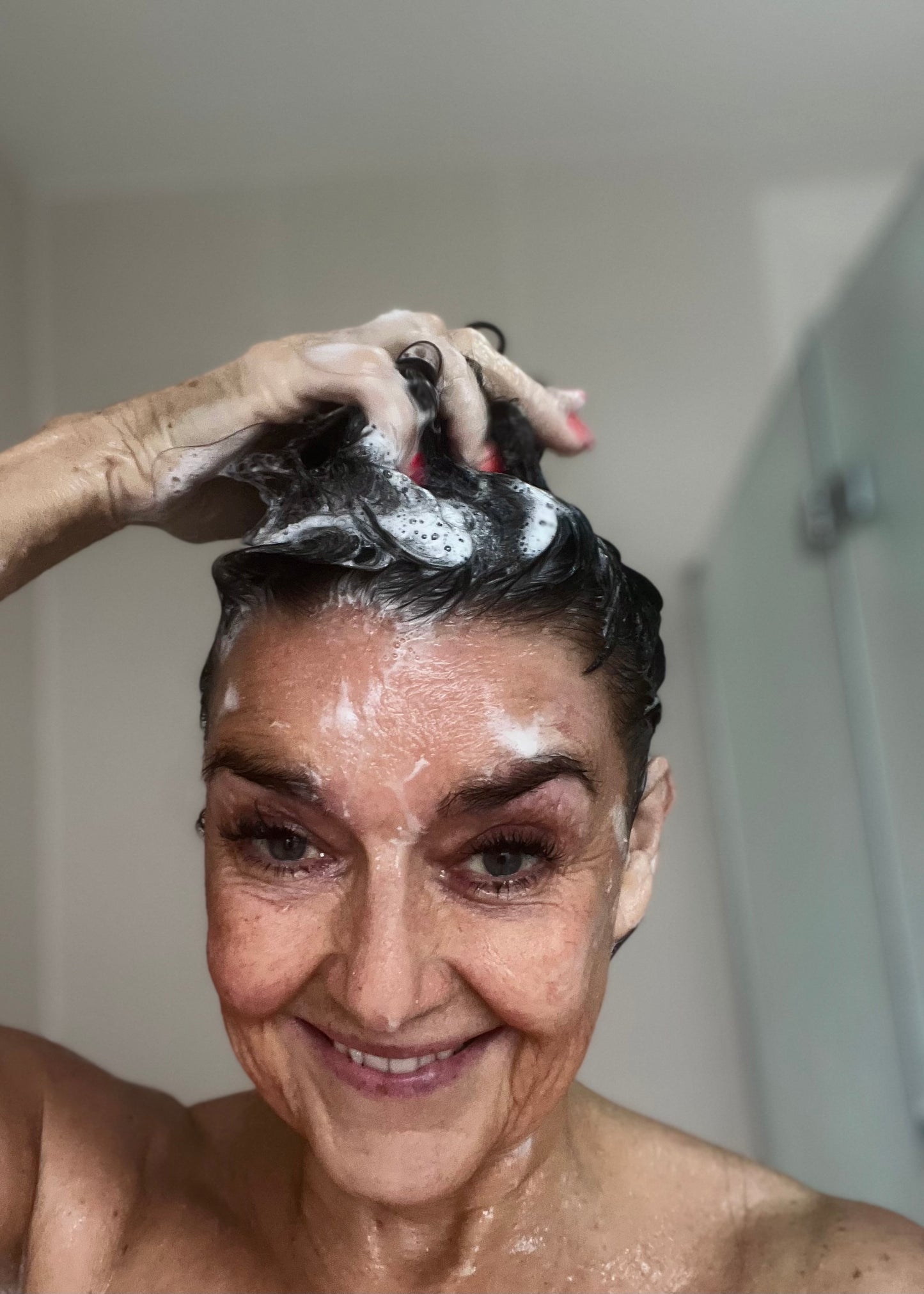 Woman applying solid shampoo to her hair with a smile showing the lather of the shampoo bar