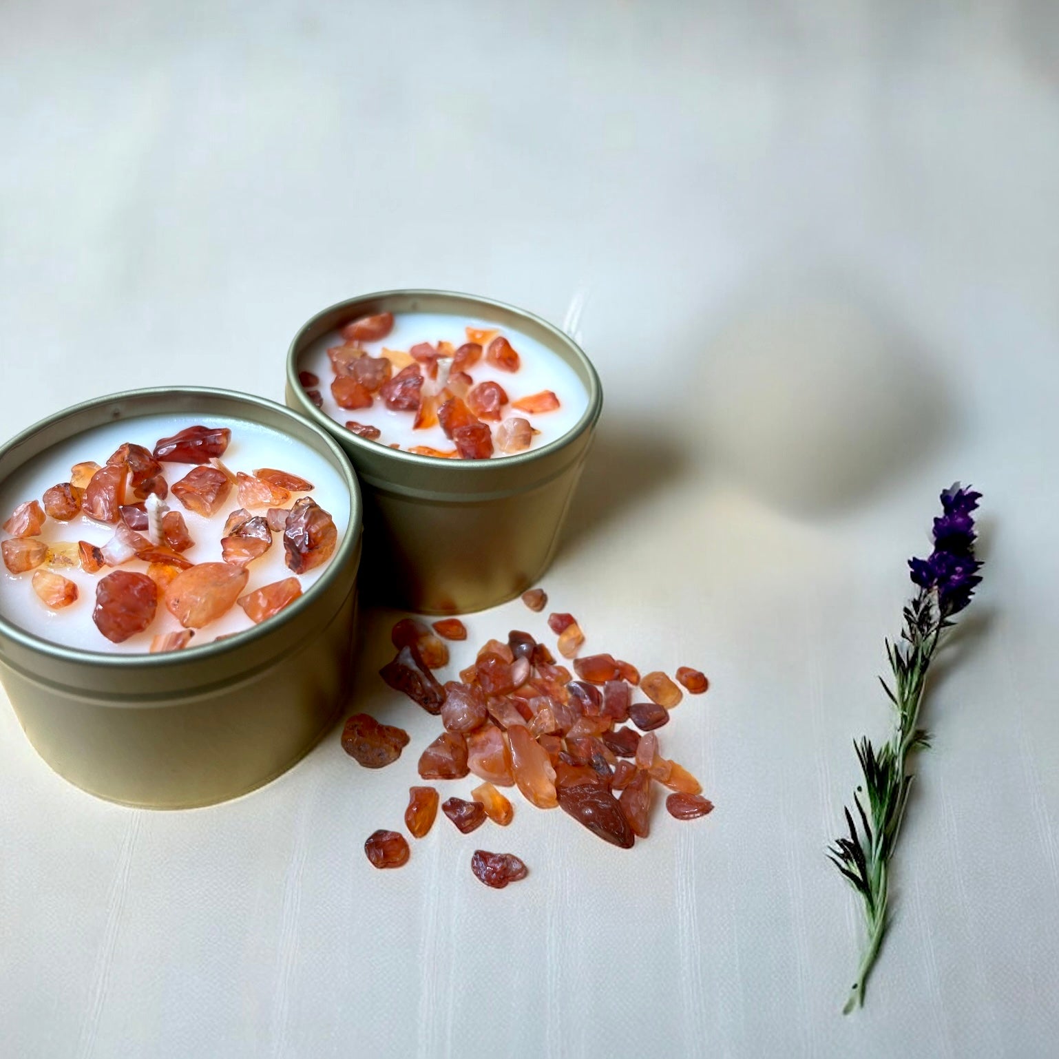 Two small containers with a white substance and carnelian crystals, accompanied by a sprig of lavender on a light background.