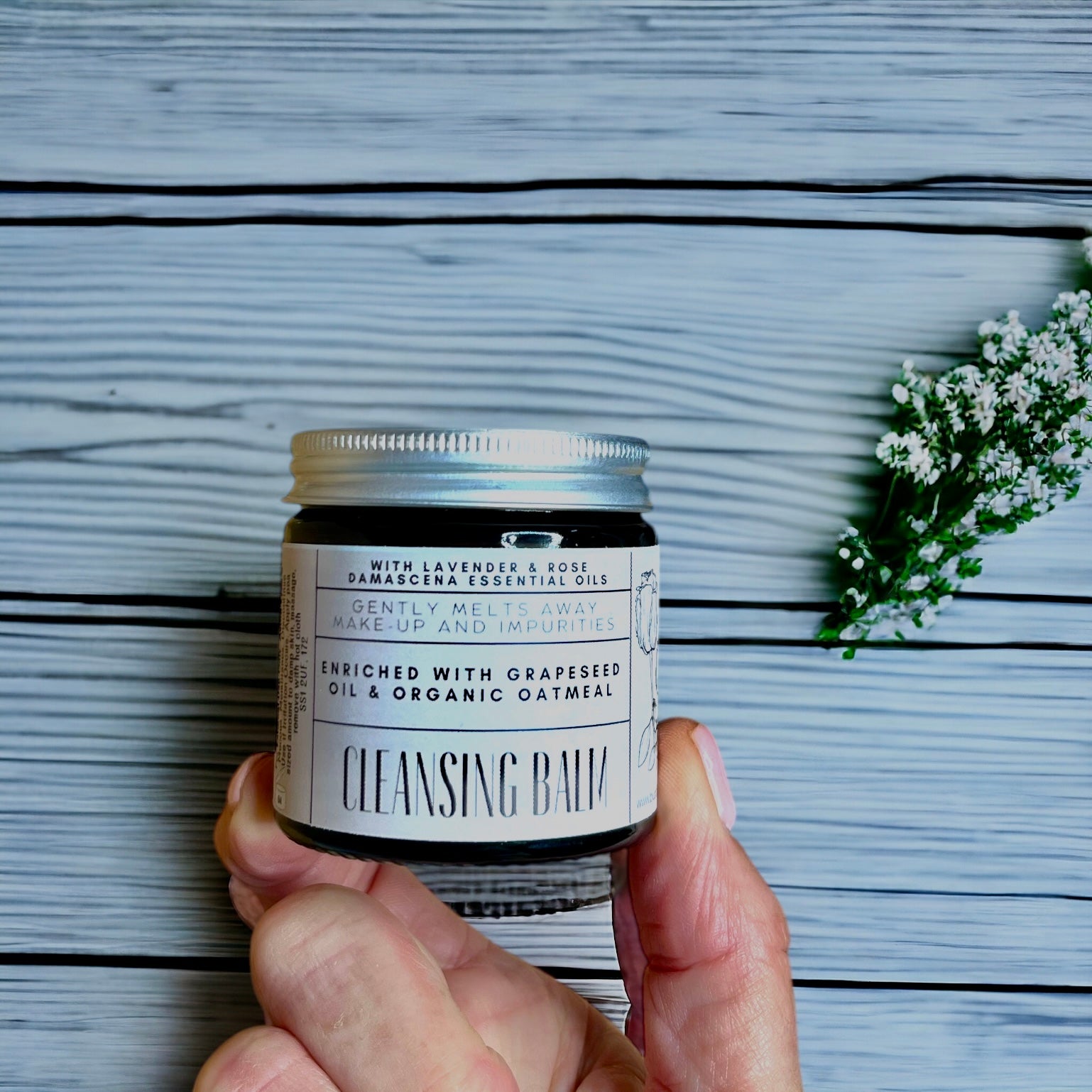 featuring a hand holding an amber glass jar of cleansing balm made with oats and lavender and rose Damascena essential oils made by buddha and bubbles botanicals