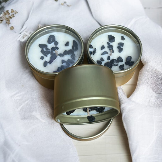 Three small gold tins crystal candles inside on a white fabric background