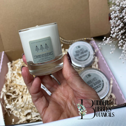 Hand holding a votive candle with 'Buddha Bubbles Botanicals' branding in a box with other beauty and haircare products.