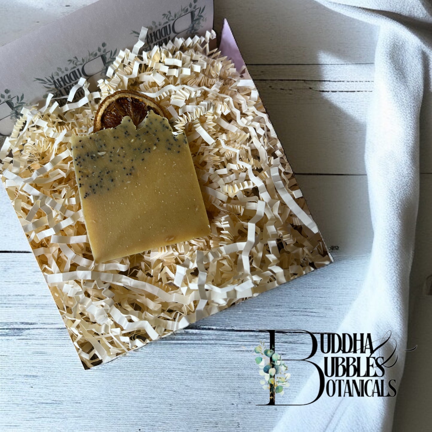 Bar of sunkissed fields soap on shredded paper with 'Buddha Bubbles Botanicals' branding on white wood