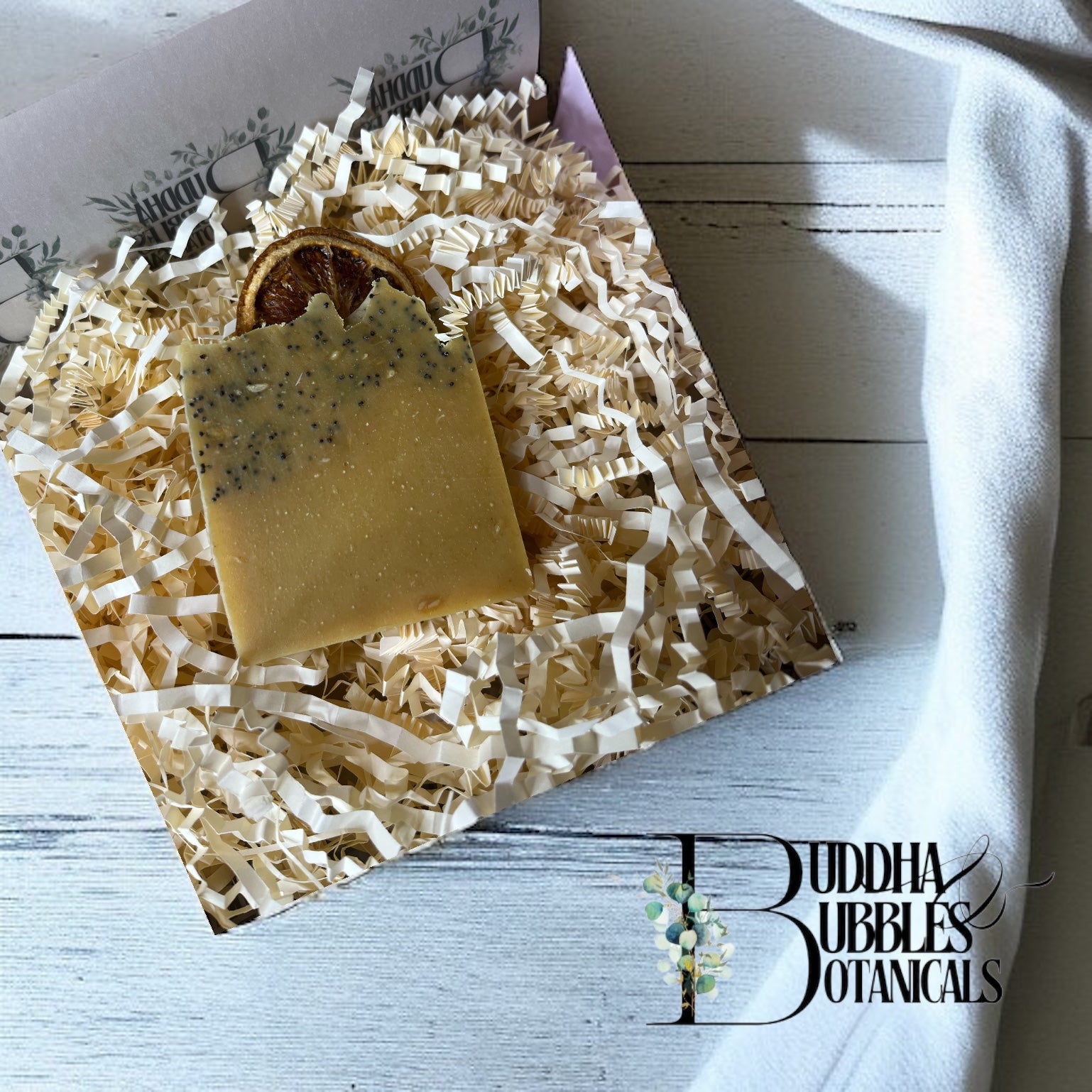 Bar of sunkissed fields soap on shredded paper with 'Buddha Bubbles Botanicals' branding on white wood