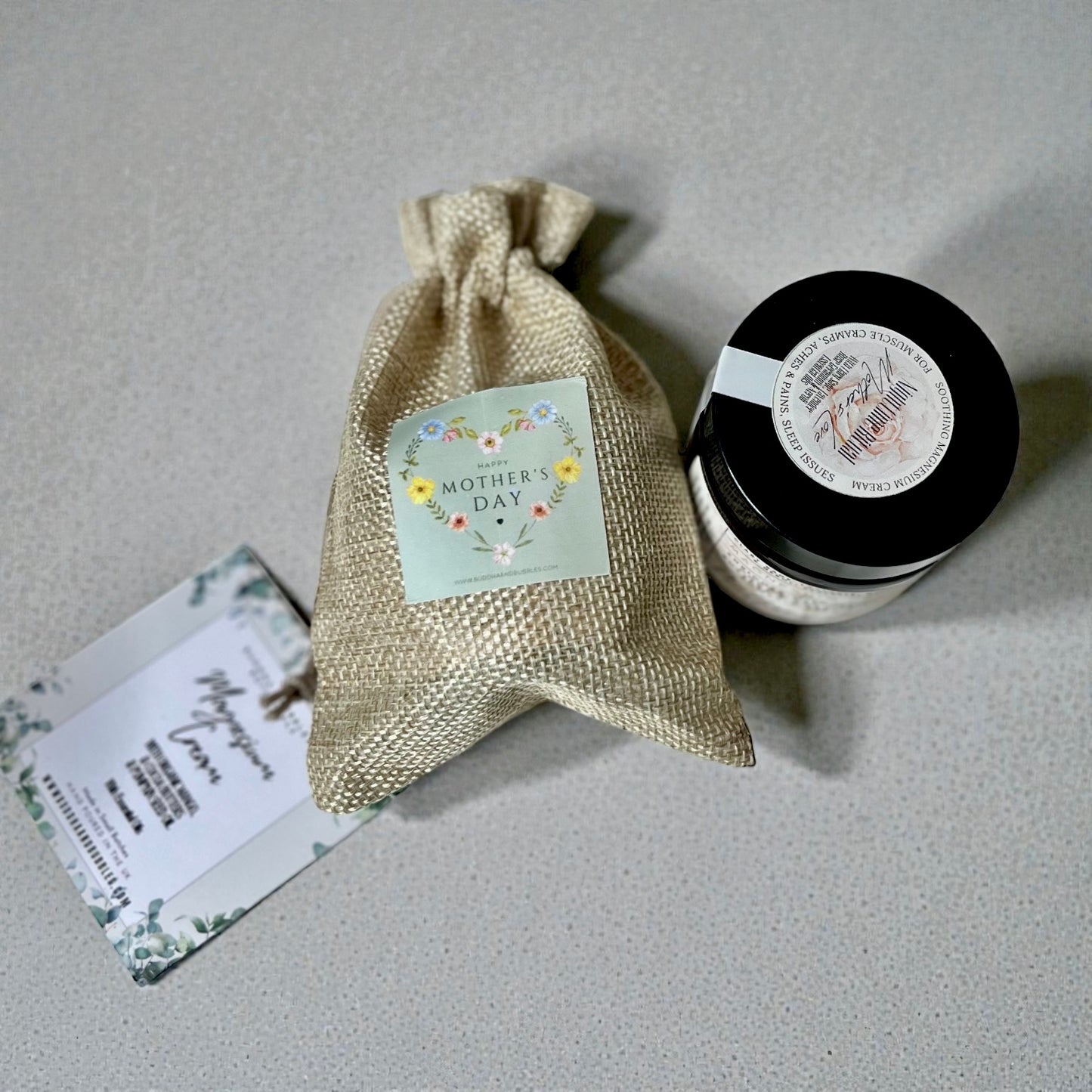 Small jar with a decorative label, burlap drawstring bag, and card on a gray surface