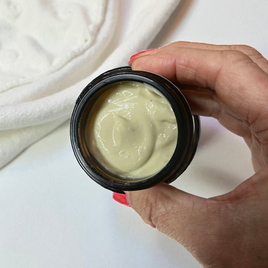 Hand holding a black container of magnesium cream for restless legs aches and pains muscle cramps  against a white background