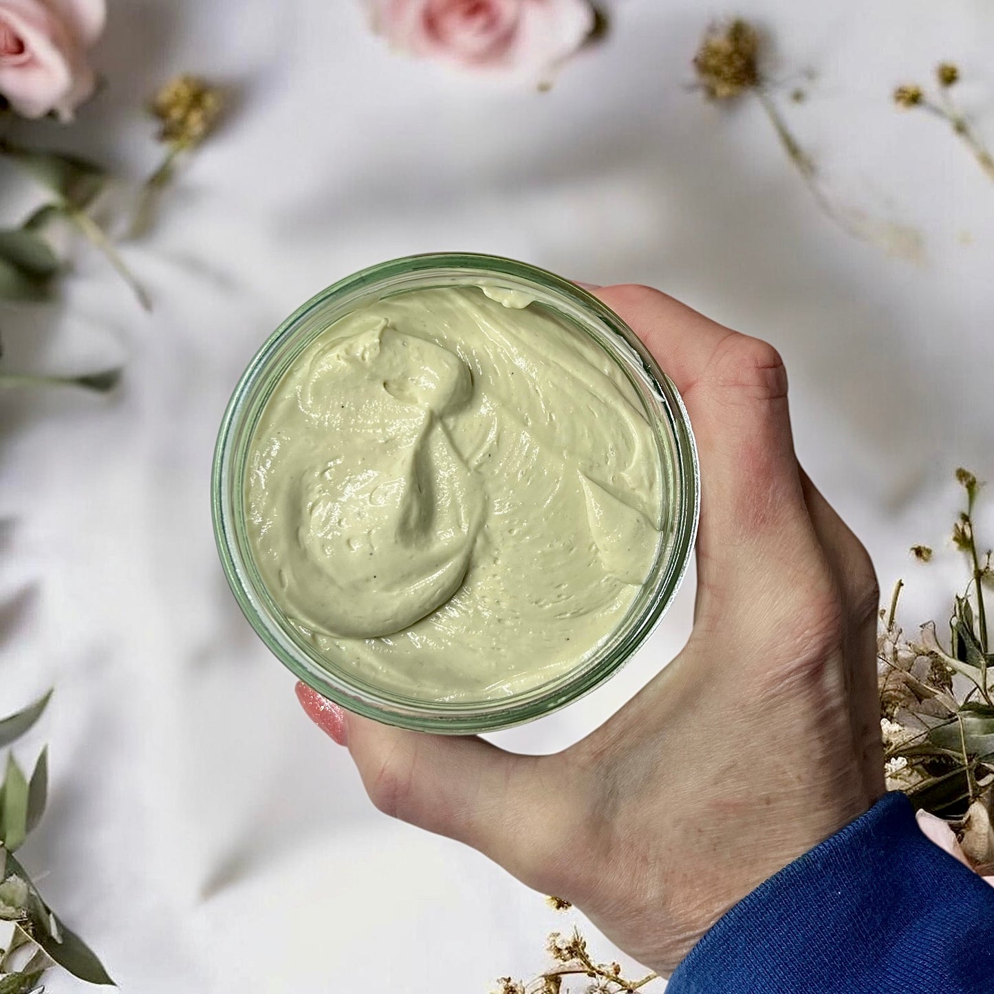 Hand holding a jumbo size jar of magnesium cream with flowers in the background