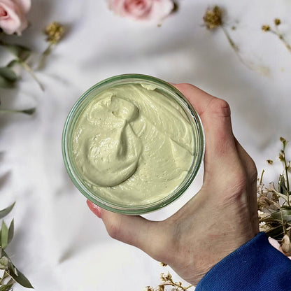 Hand holding a jumbo size jar of magnesium cream with flowers in the background