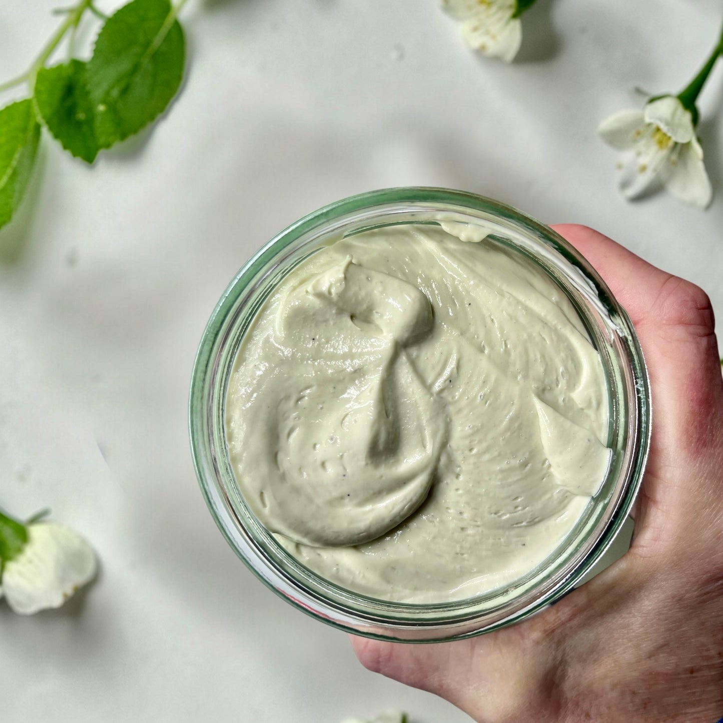 hand holding a jumbo Jar of magnesium cream placed on a soft white surface.
