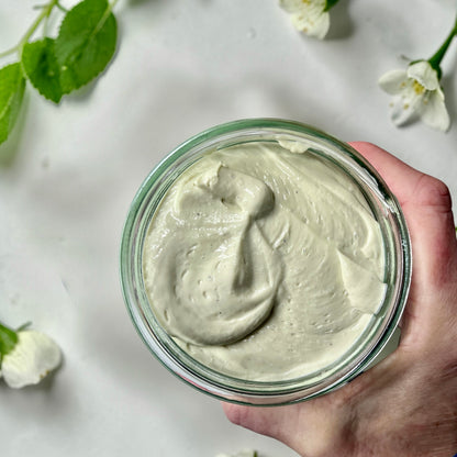 hand holding a jumbo Jar of magnesium cream placed on a soft white surface.