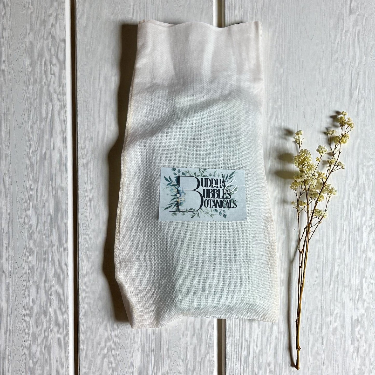White linen bag with wax melt snap bar with 'Buddha Bubbles Botanicals' logo on a light wooden surface.
