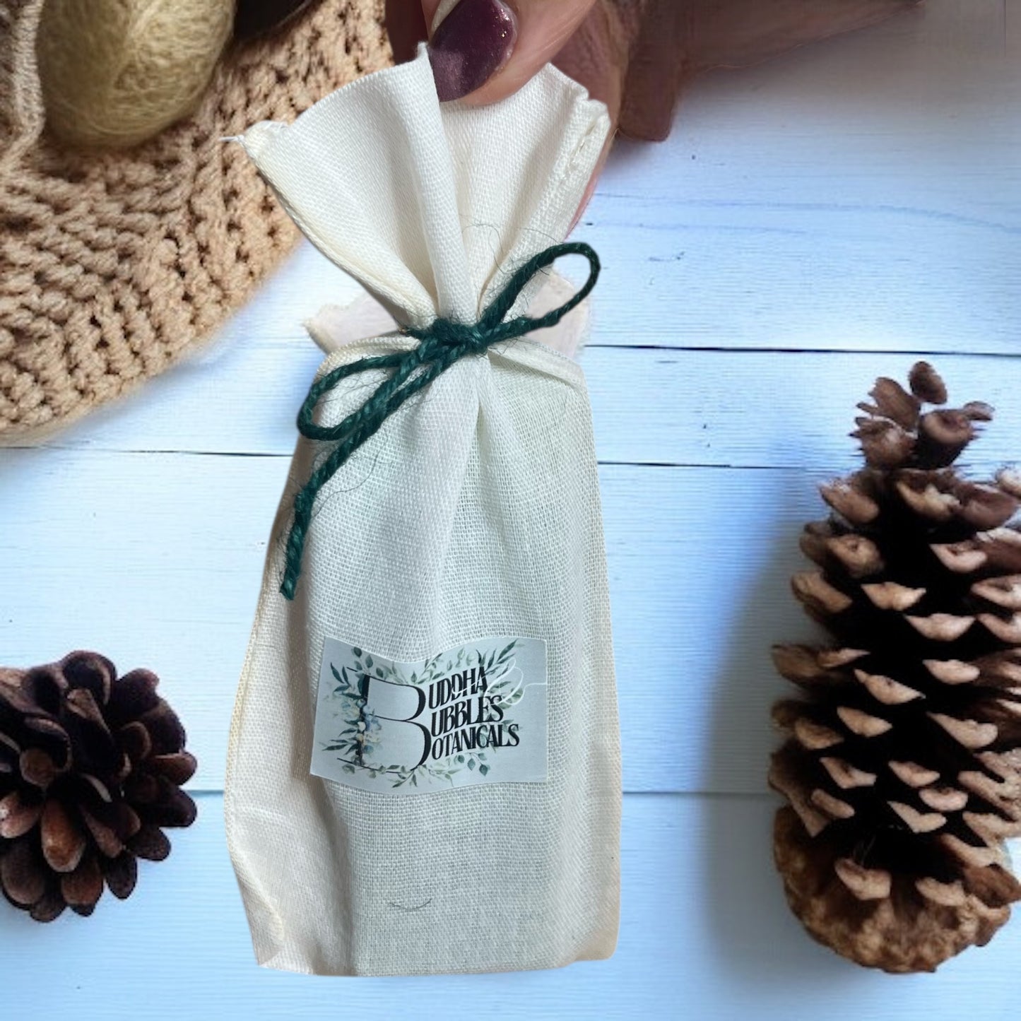 Wax Melt snap bar wrapped in a cotton drawstring bag with a label, surrounded by pinecones on a light wooden surface