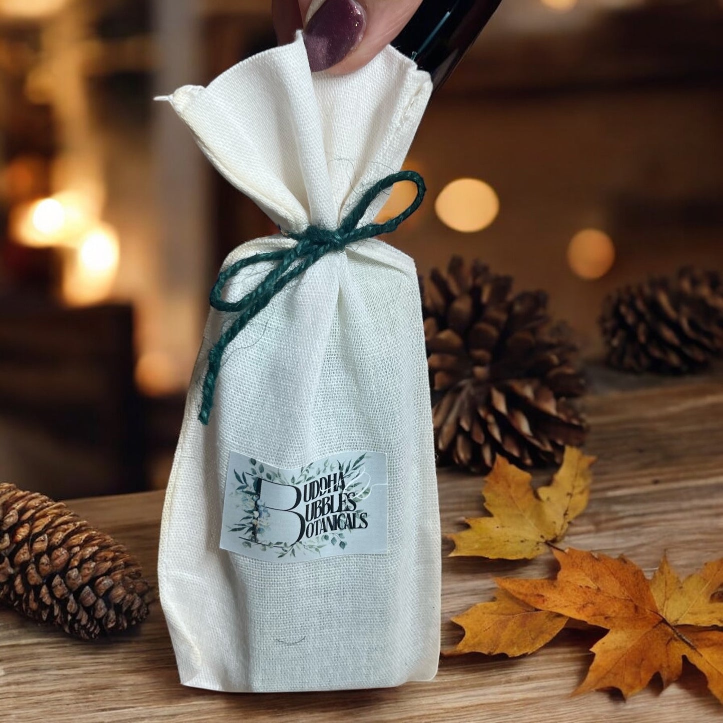 White drawstring bag containing wax melt snap bar with a label on a wooden surface with pinecones and leaves.