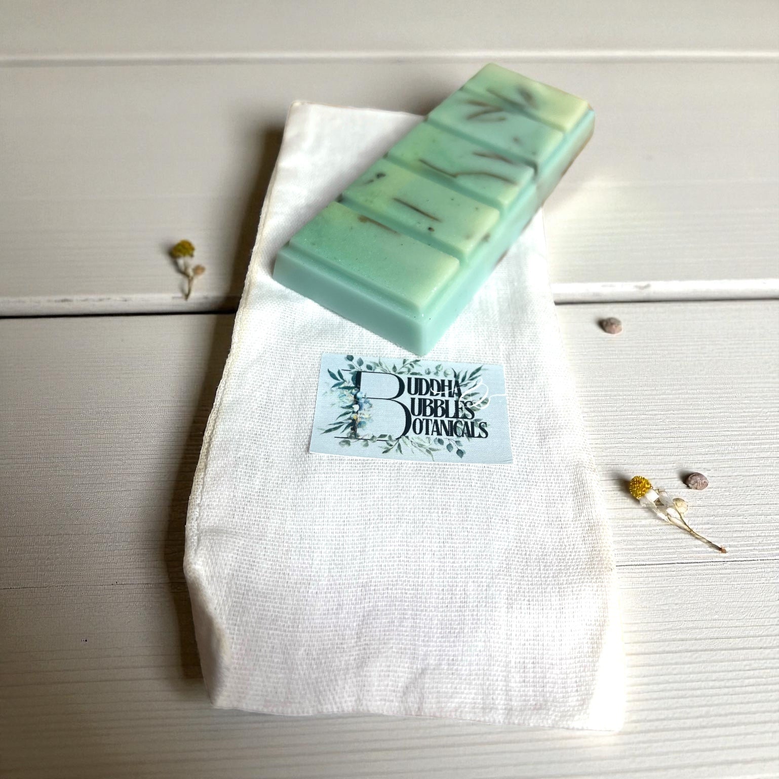 Green wax melt snap  bar on a white cloth with 'Buddha Bubbles Botanicals' branding on a wooden surface.