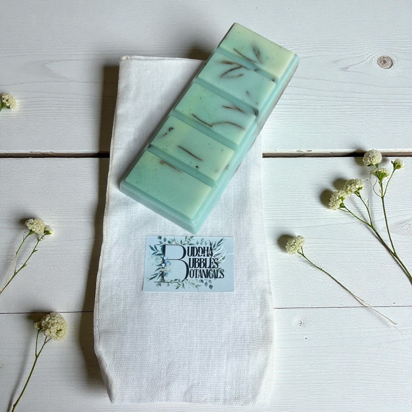Green wax melt snap bar on a white cloth reusable bag with dried flowers on a wooden surface