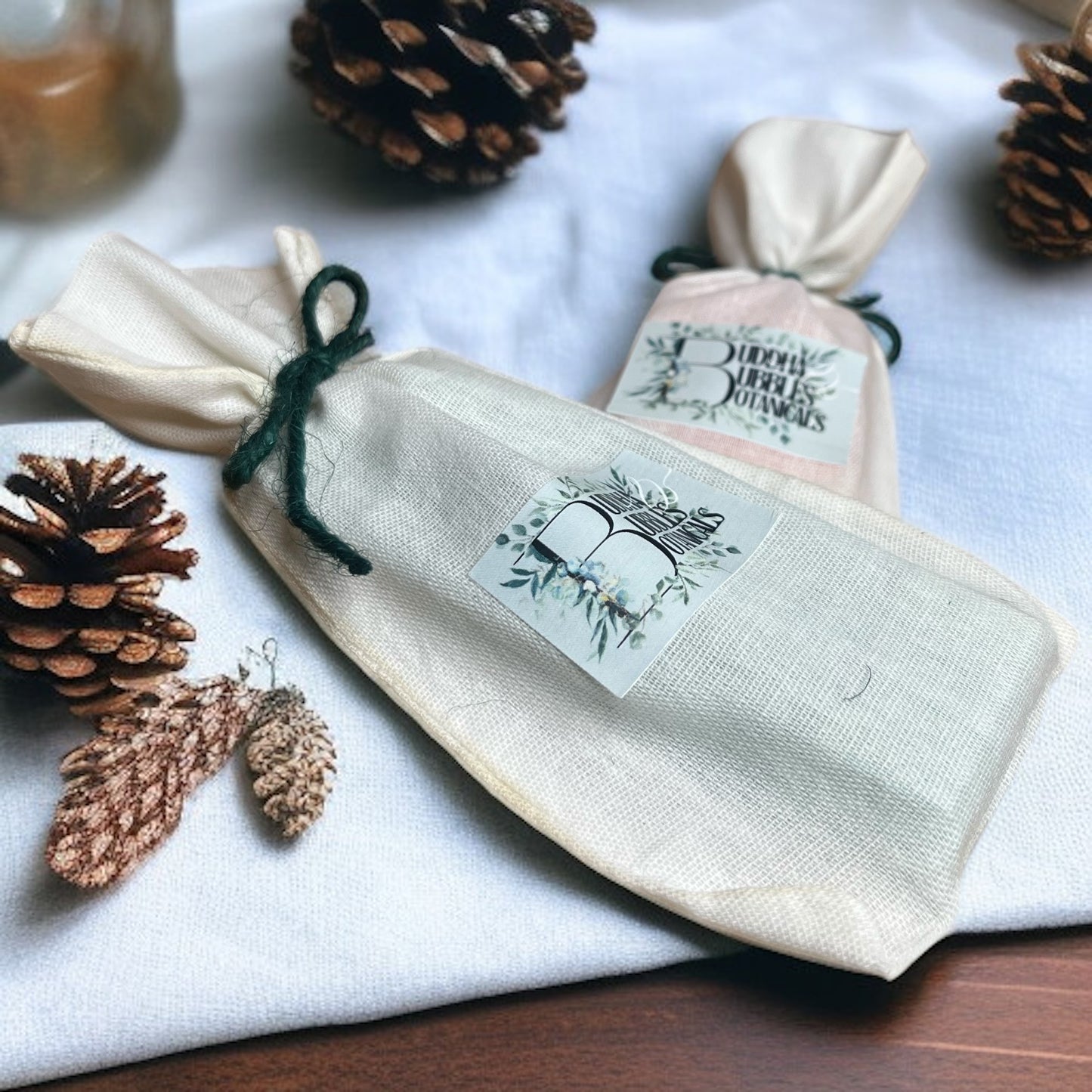reusable bag containing wax melt snap bar with a label, surrounded by pine cones and leaves on a white surface.