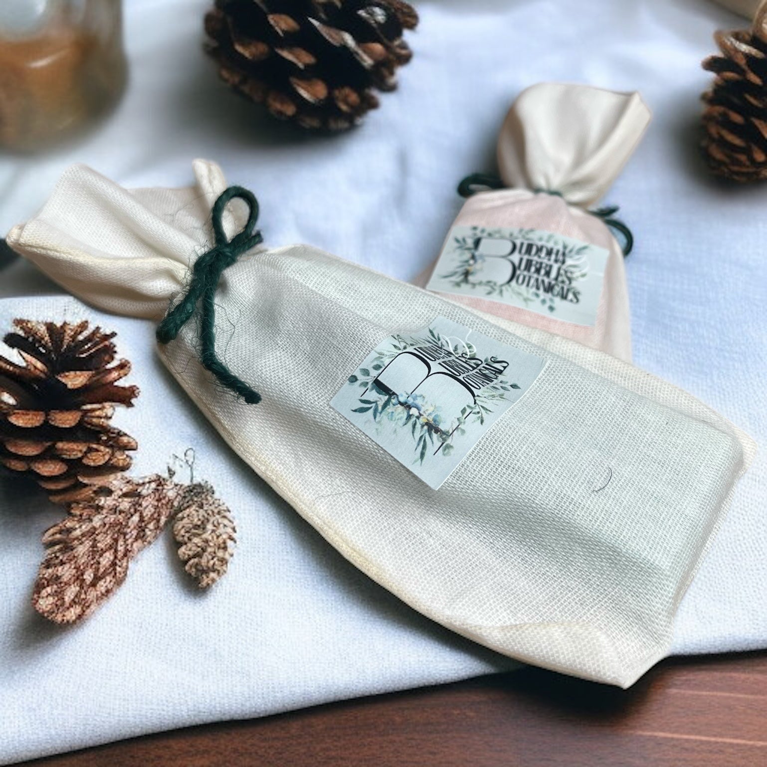 reusable bag containing wax melt snap bar with a label, surrounded by pine cones and leaves on a white surface.