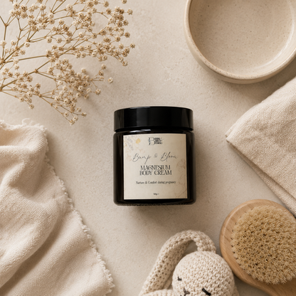 A jar of Bump & Bloom Magnesium Body Cream is styled in a flat-lay arrangement on a textured beige surface with dried flowers, a small bowl, a folded cloth, a wooden scrubber, and a knit towel.
