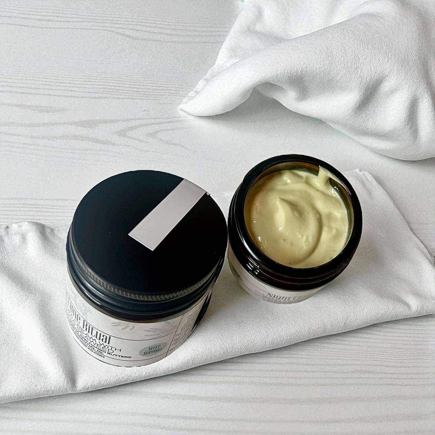 Two jars of magnesium cream one with lid off with Irish moss seaweed  on a white surface 