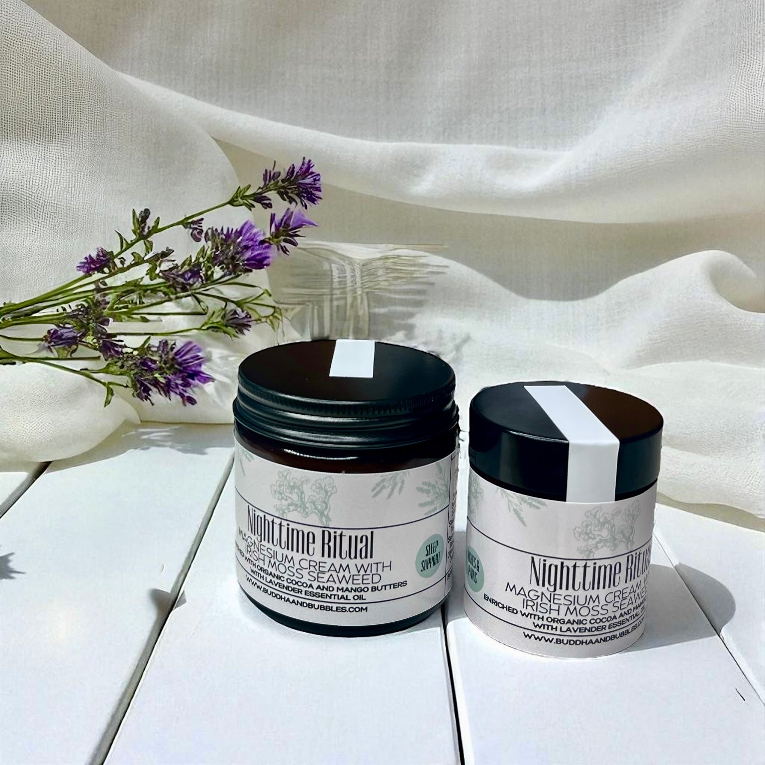 Two jars of 'Nighttime Ritual' magnesium cream with Irish moss seaweed on a white surface with lavender flowers.