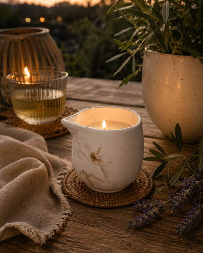 massage Candle in a ceramic candle holder, glass of liquid, and lavender on a wooden surface.